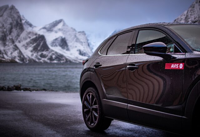 an avis car parked on a road by water and mountains