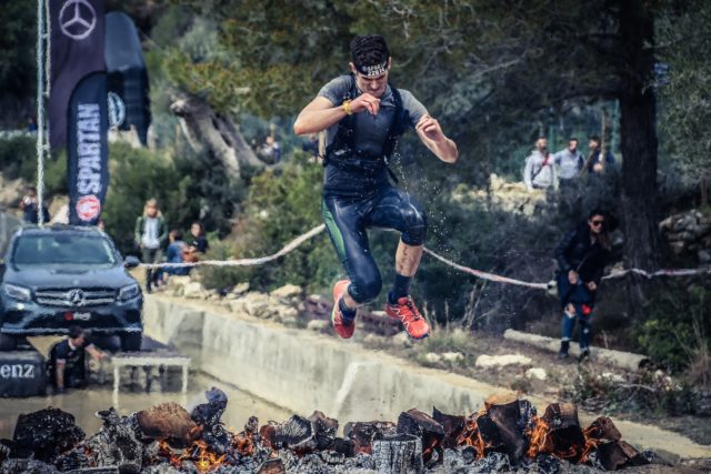 man jumping on flaming charcoal during spartan race